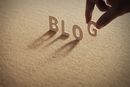 Fingers adding a wood letter "g" to the word "blog" 